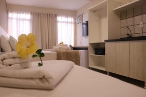 Camera d'albergo con un letto, un tavolino con asciugamani, una finestra con tende, una TV a muro e un angolo cottura.