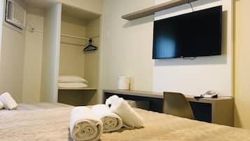 A hotel room with a bed, a desk, a chair, a TV, a wardrobe, and a shower area.
