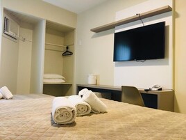 Una camera d'albergo con un letto, una scrivania, una sedia, una televisione, un armadio e un angolo doccia.