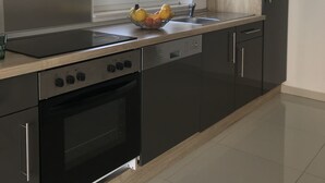 A modern kitchen with a built-in oven, a stovetop, and a dishwasher. There is a window above the sink, and a fruit bowl on the counter. - Bella Casa Srima Comfort  (Vodice)