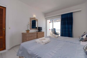 A bedroom with a bed, a television, a dresser, and a view of the beach through the window. - Club Atlantis 89 - Two Bed (Costa Adeje)
