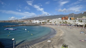 Un hôtel situé sur la côte, offrant une vue sur la plage, un port de plaisance et un paysage montagneux en arrière-plan.