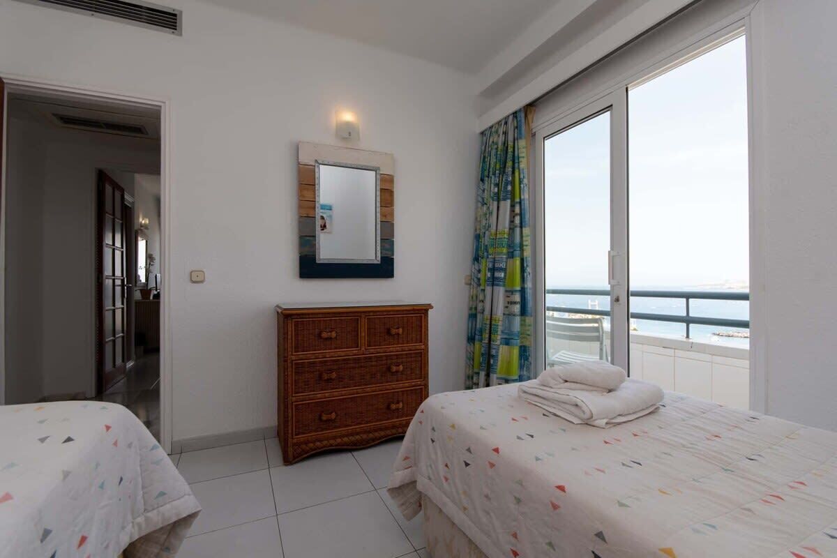 Une chambre d’hôtel avec deux lits, une commode en bois, un miroir et un balcon donnant sur la mer.