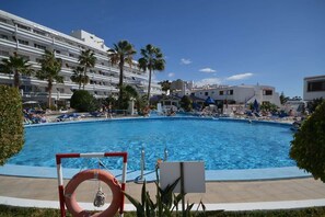 A swimming pool with lounge chairs and palm trees, surrounded by buildings. - Club Atlantis 89 - Two Bed (Costa Adeje)