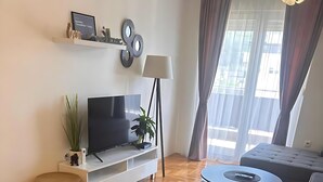 Un salon moderne avec un téléviseur à écran plat, un canapé, une table à manger avec des sets de table et une plante en pot.