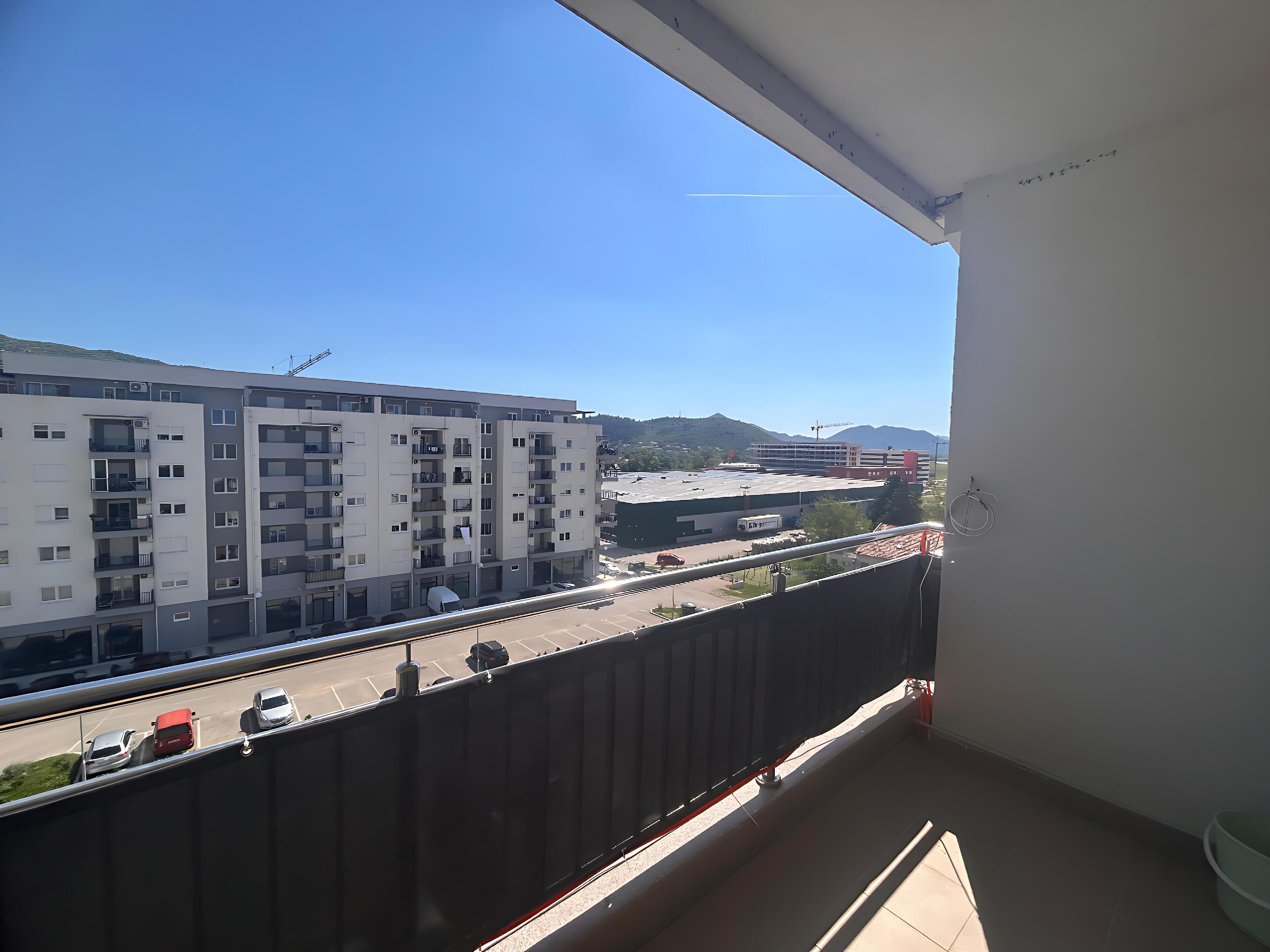 Een balkon met uitzicht op een meerhoog gebouw, een parkeerplaats en verre bergen.