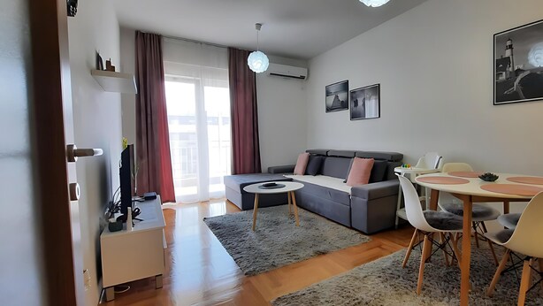 Un salon moderne avec un canapé gris, une petite table ronde et un coin repas comprenant une table blanche et des chaises grises.