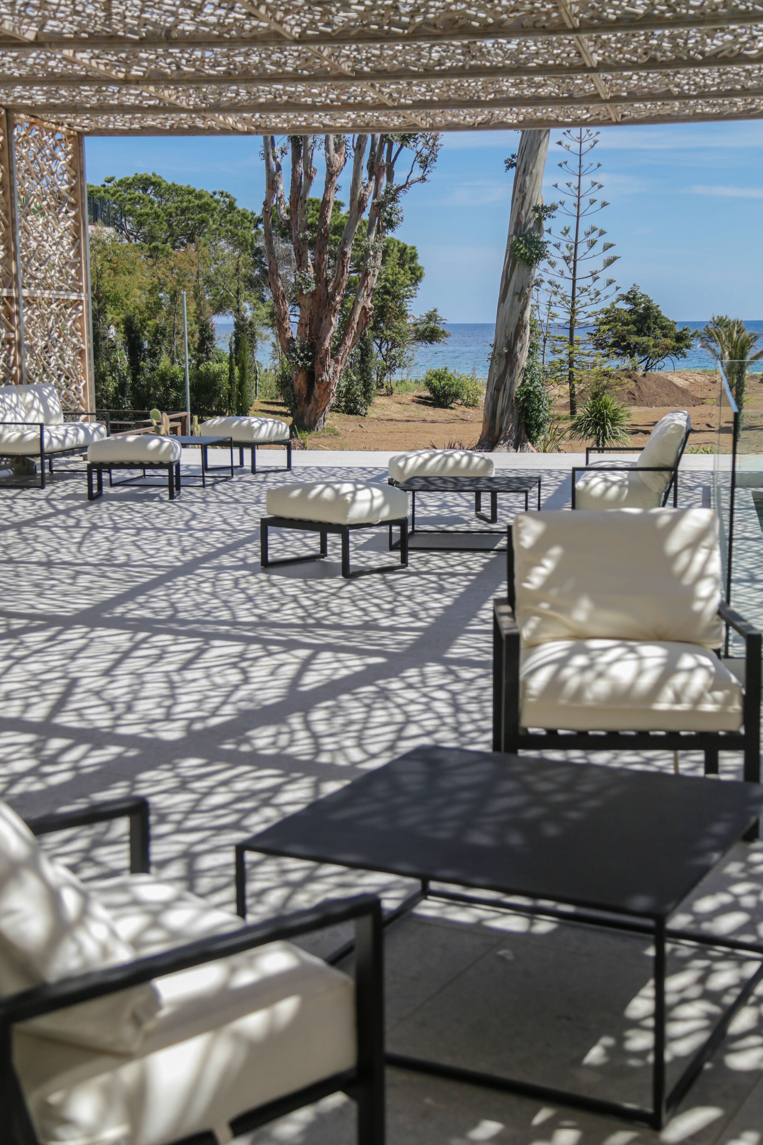 Un área de estar al aire libre con mesas y sillas, una pérgola encima y vista a la playa y al océano.