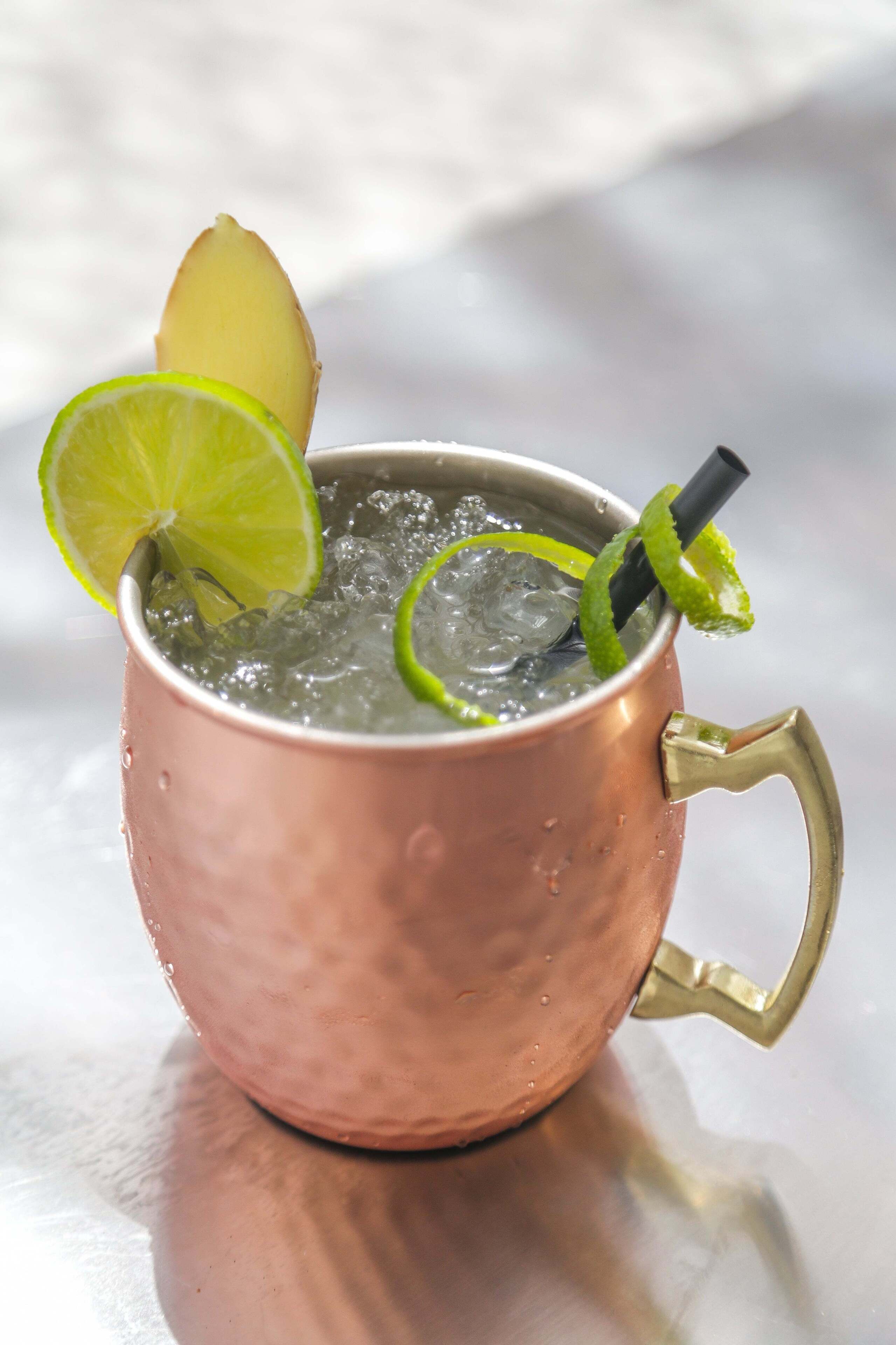 A copper mug with a handle, filled with ice and garnished with lime slices and a lime wedge.