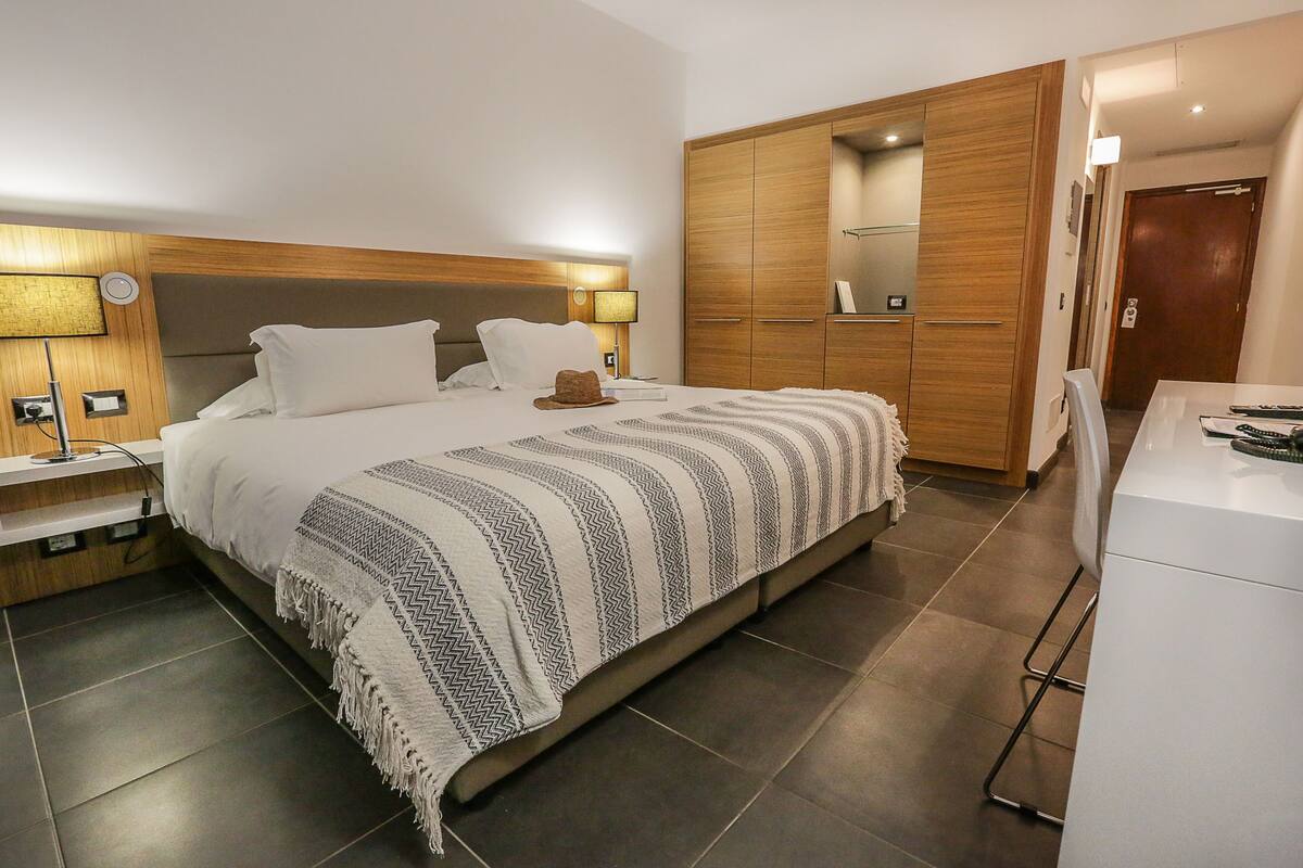 Une chambre d’hôtel moderne avec un grand lit, une armoire en bois et un bureau avec une chaise.