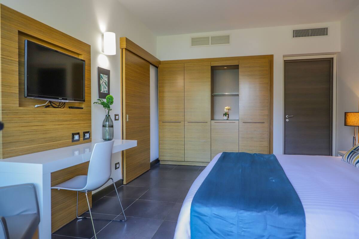 Une chambre d’hôtel moderne équipée d’un lit, d’un bureau, d’une chaise, d’une télévision et d’une armoire.