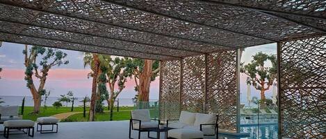 Un espace extérieur abrité avec des places assises, offrant une vue sur la piscine, doté d’un plafond en treillis et de mobilier d’extérieur.