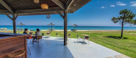An outdoor seating area with tables and chairs overlooking a beach.