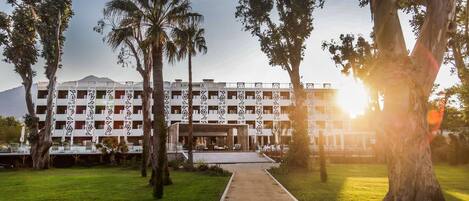A hotel with a central courtyard, palm trees, and a mountain in the background.