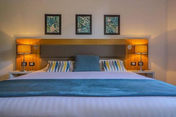 A neatly made bed with a blue blanket, two bedside lamps, and three framed artworks on the wall above. - Hotel Restaurant San Lucianu (San-Nicolao)