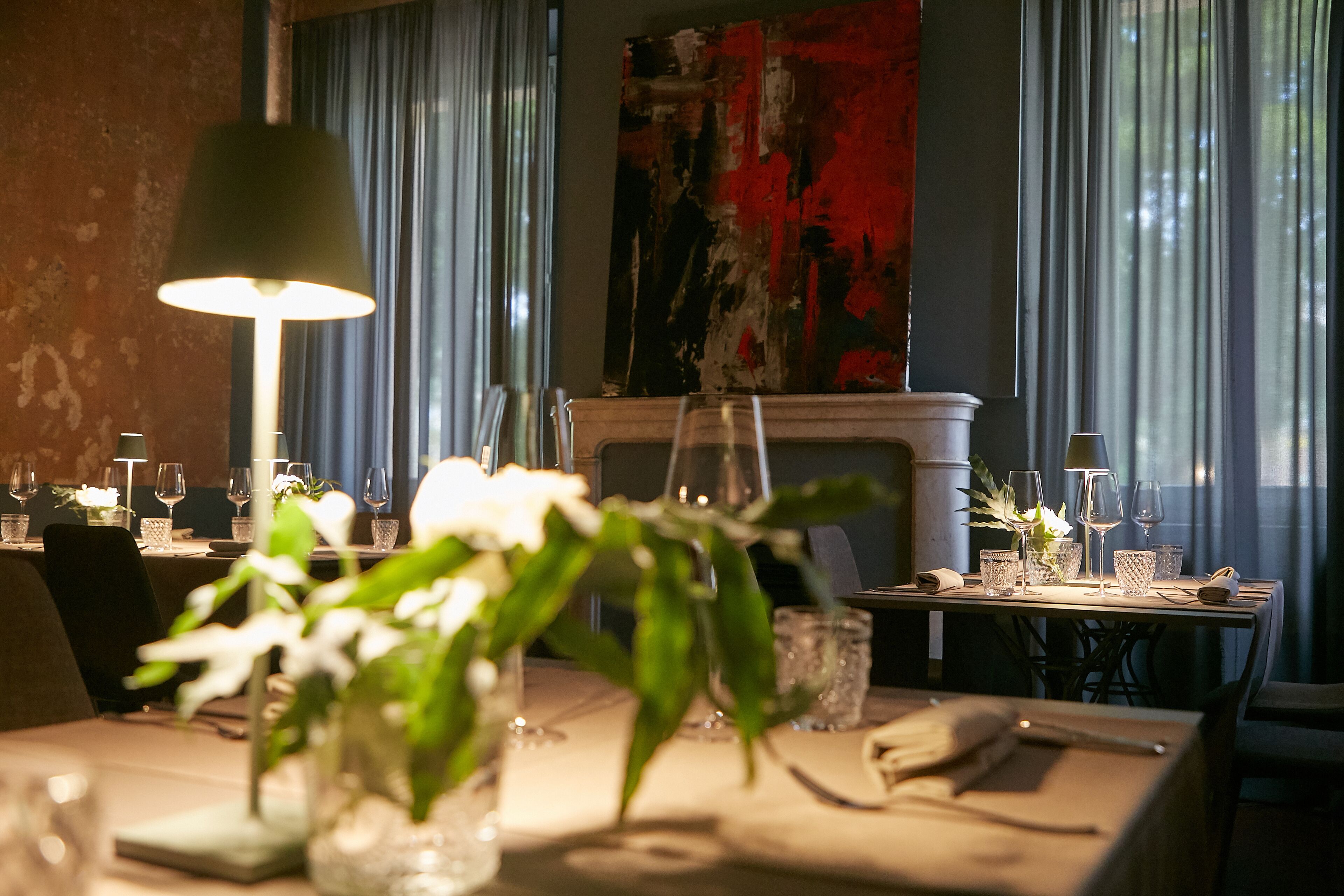A dining area with tables set for two, featuring glassware and a vase with flowers.