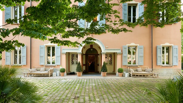 A building with a cobblestone courtyard, a central archway, and two seating areas with potted plants. - Mery Bistrot in Villa Bisbini (Marano sul Panaro)