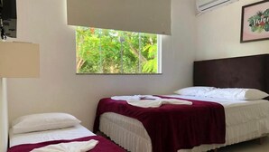Habitación de hotel con dos camas, cada una con colcha blanca y color burdeos, y un ventanal con vistas a zonas verdes.