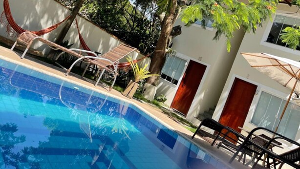 Una piscina con una hamaca y sillas de descanso, rodeada de árboles y un edificio.