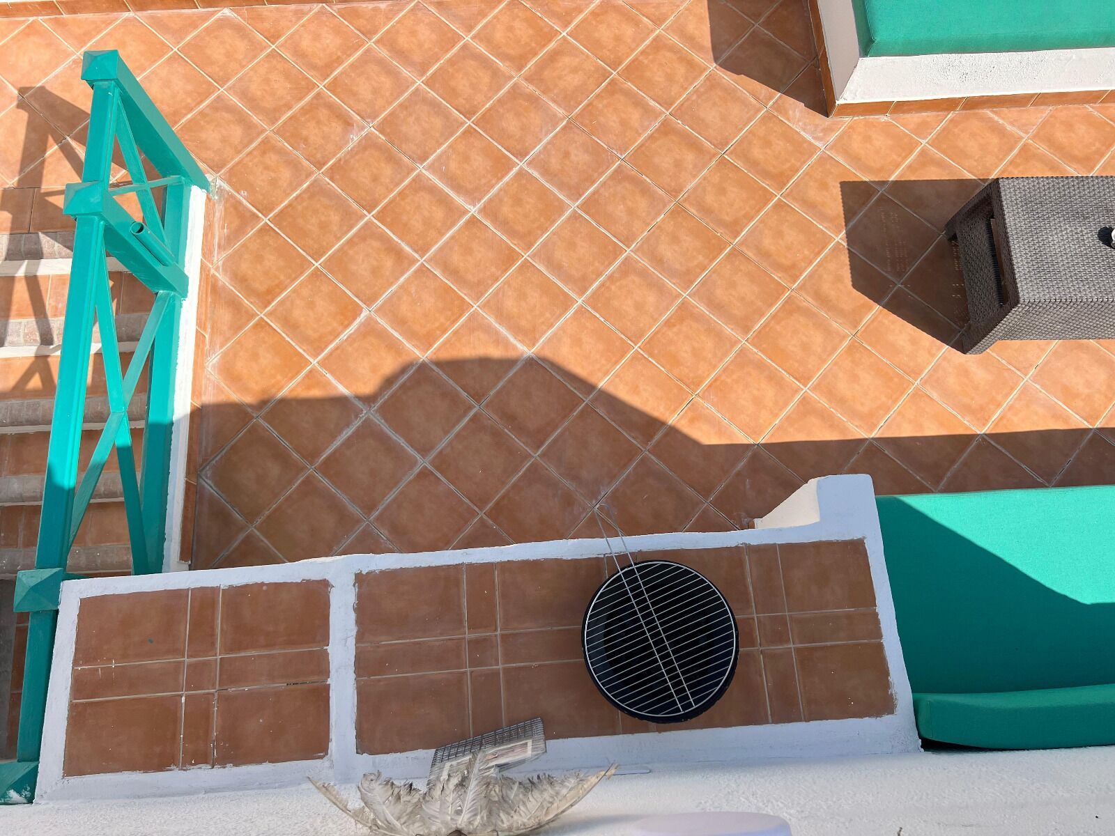A tiled wall with a metal grill, a green ladder, and a white structure.