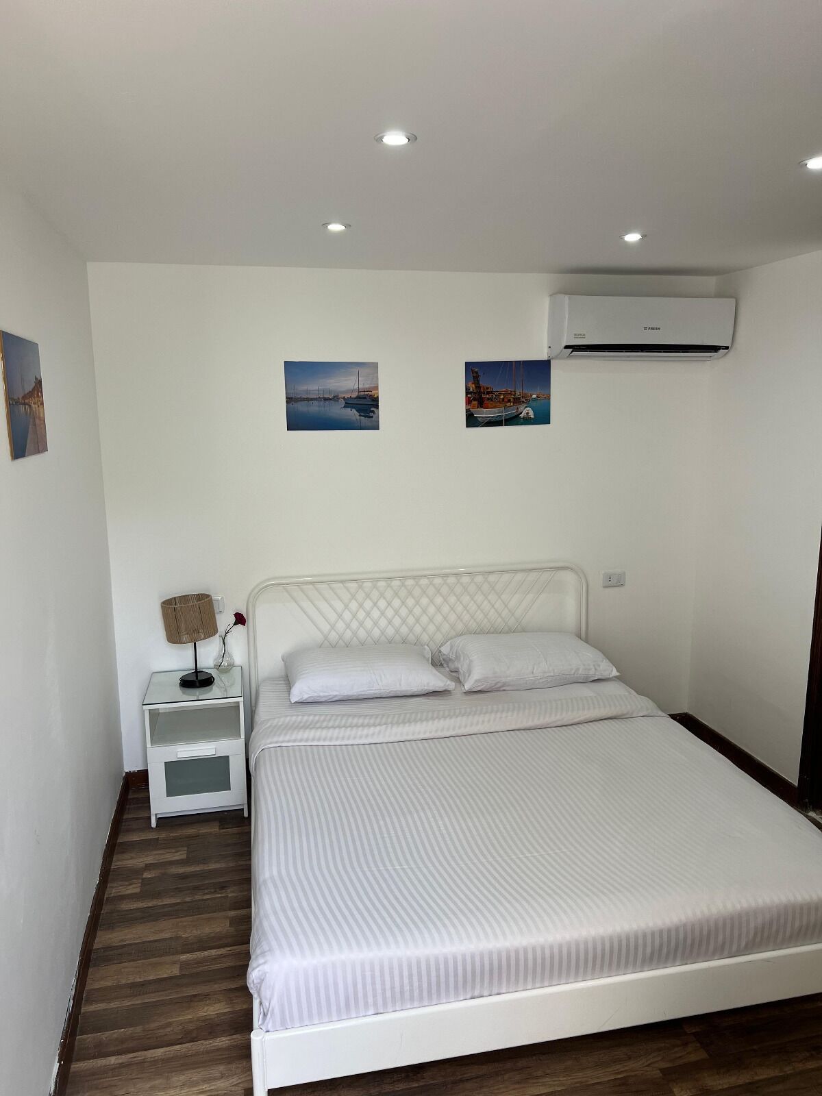 Un dormitorio con cama, mesitas de noche blancas, una lámpara y dos unidades de aire acondicionado instaladas en la pared.
