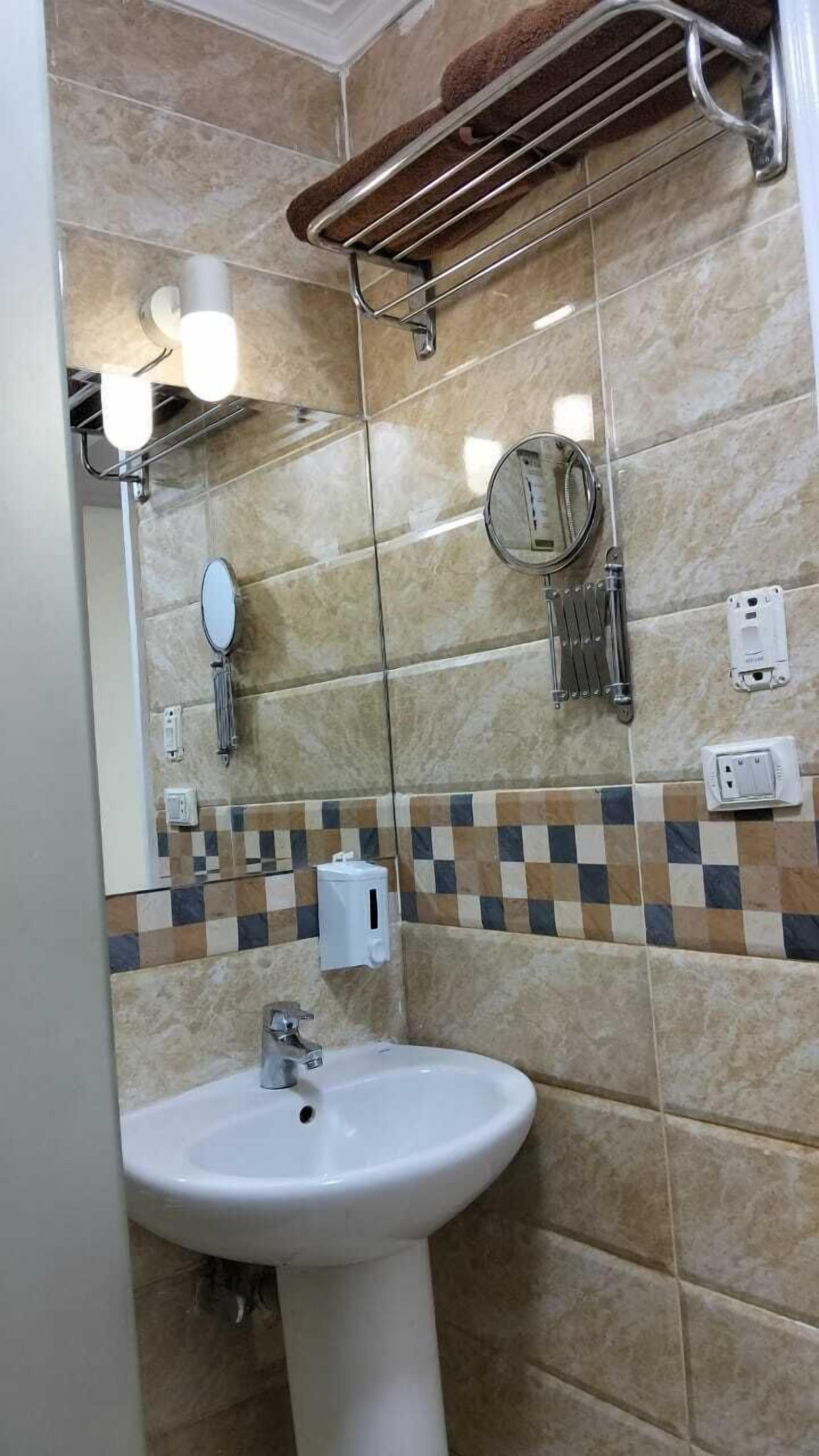 Egy fürdőszoba, melyben fehér mosdókagyló, tükör, törölközőtartó és csempézett fal található.