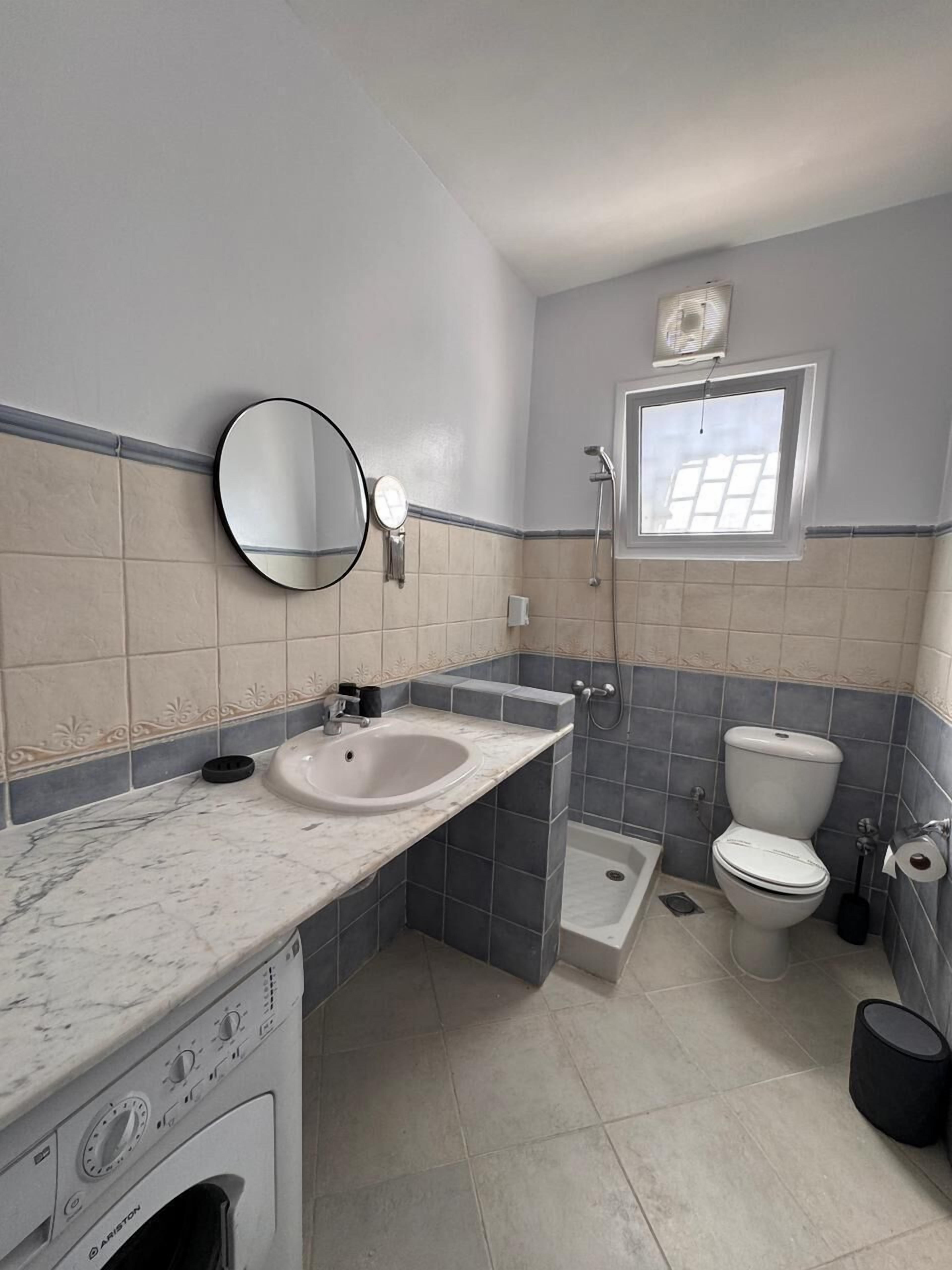 A bathroom with a sink, mirror, toilet, shower, and a window.