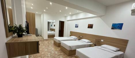 A modern hotel room with a large bed, a smaller bed, a desk, and a bathroom visible through an open door.