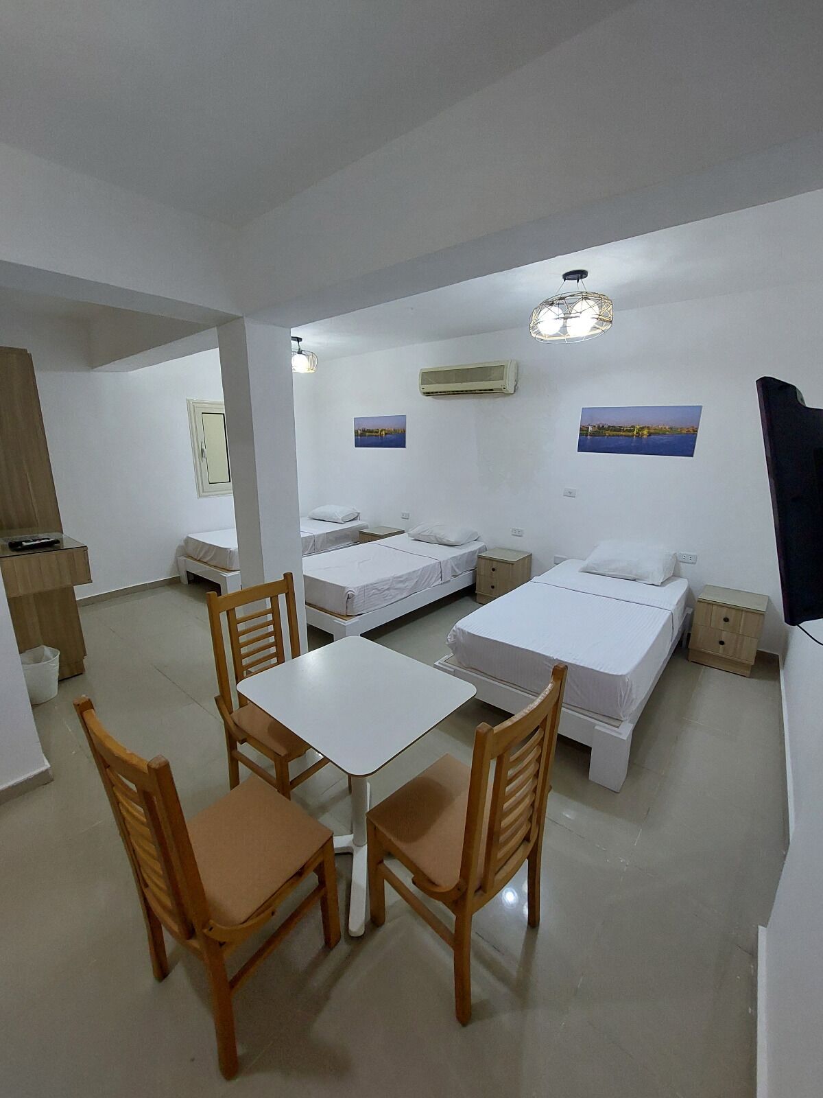 Una habitación con una mesa de comedor, cuatro sillas, dos camas individuales, un televisor y dos aires acondicionados instalados en la pared.