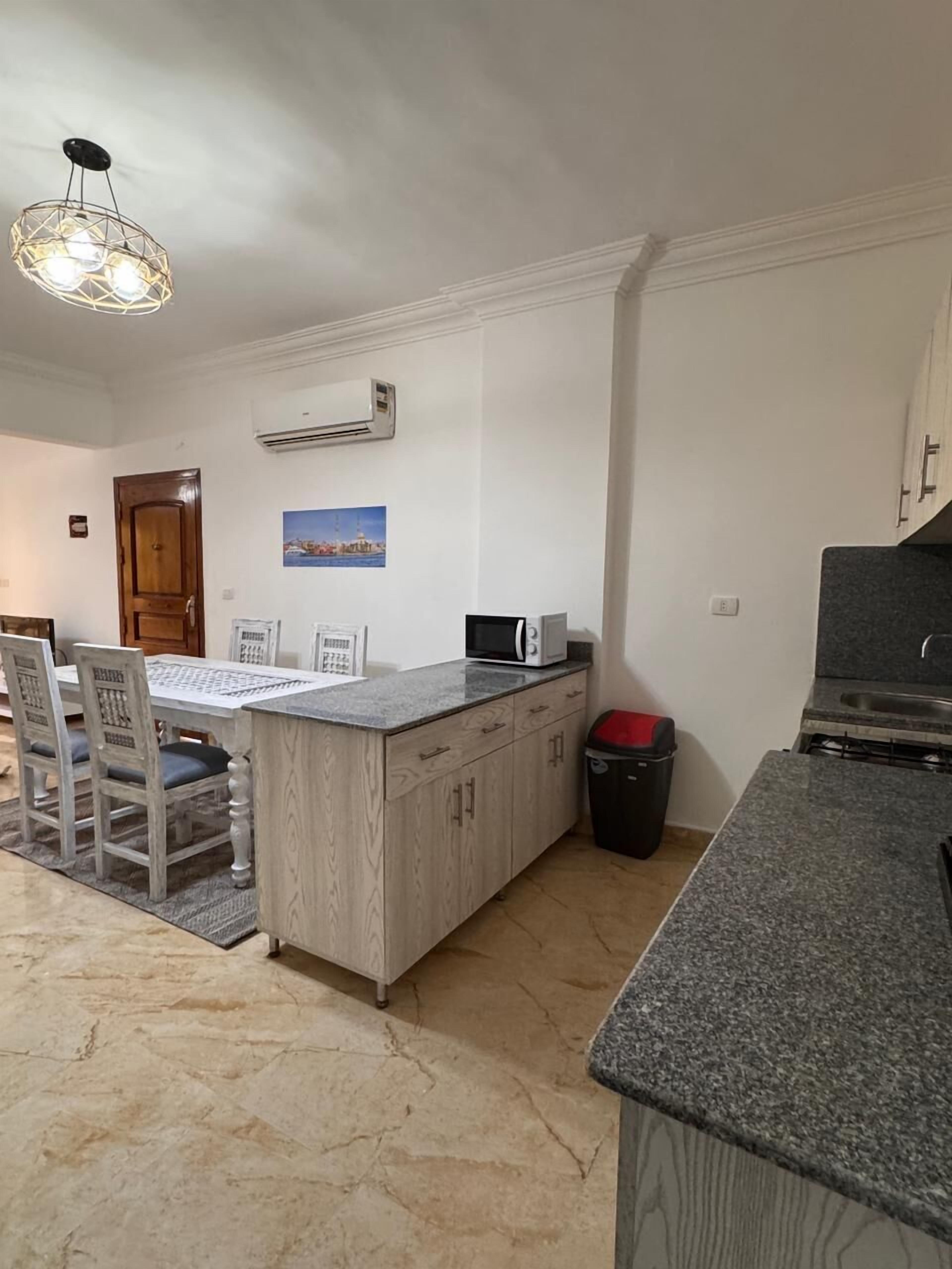 A kitchen with a granite countertop, a microwave, a stove, and a dining area with a wooden table and chairs.