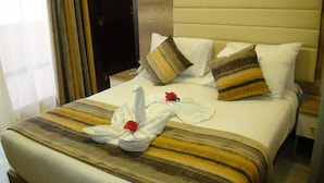 Camera d'albergo con un letto, cuscini, una coperta e un asciugamano con una rosa.