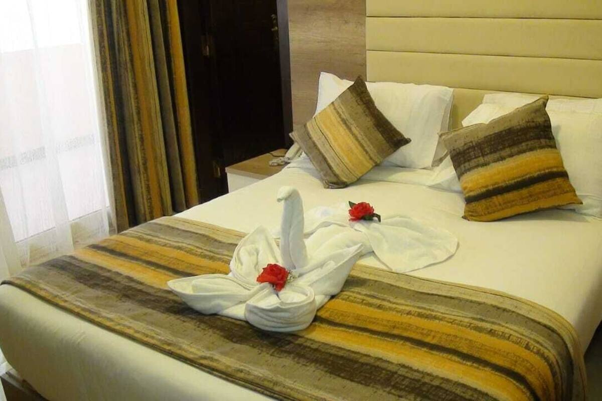 Una habitación de hotel con cama, almohadas, una colcha y una toalla con una rosa.