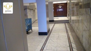 Un corridoio con una poltrona blu, una segnaletica per 'JEWEL Hotel' e pavimento in marmo.