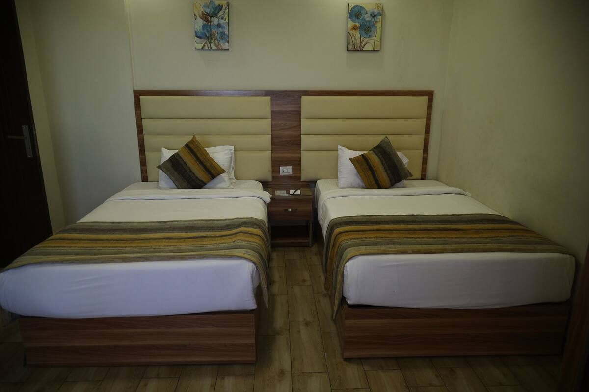Habitación de hotel con dos camas, cabeceros de madera y suelo de madera.