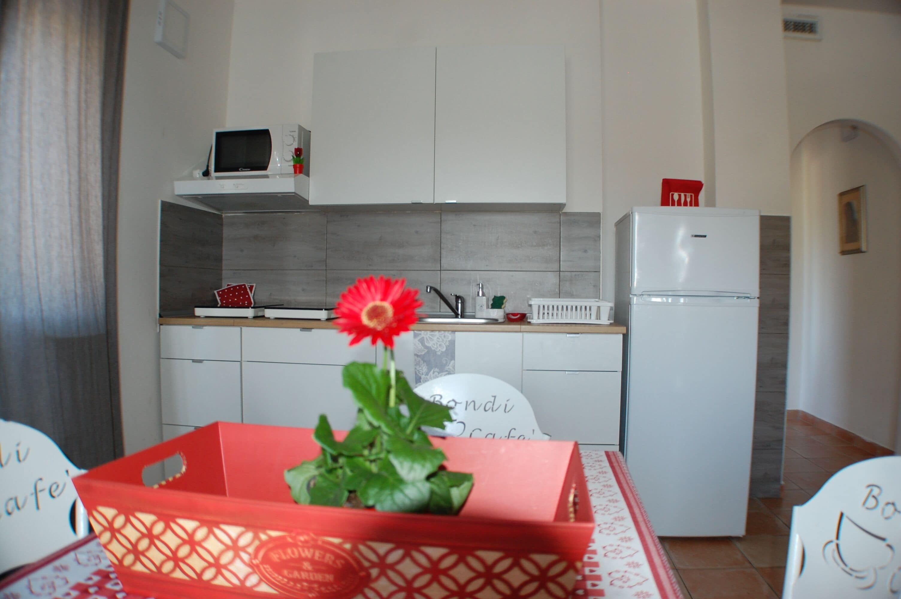 Una cocina con armarios blancos, un microondas, un refrigerador y una flor roja en una cesta.