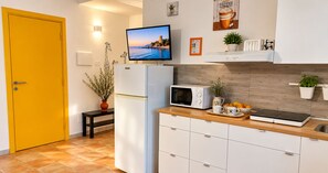 A modern kitchen with a microwave, a refrigerator, and a television on a stand. There is a wooden countertop with a cutting board and a bowl of fruit. - le casette di Frà (Tolfa)