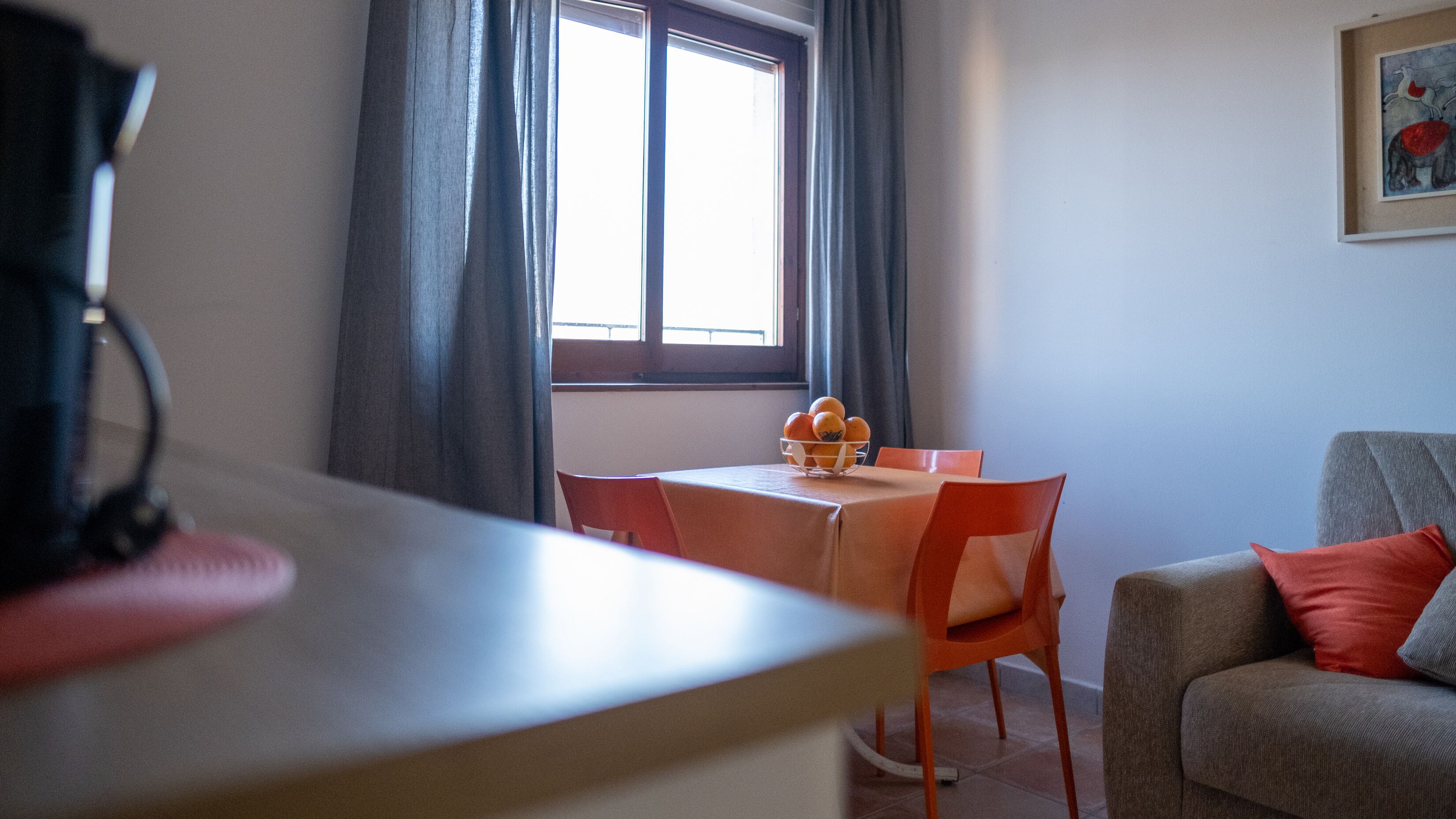 A dining area with a table, chairs, a bowl of fruit, and a window with curtains.