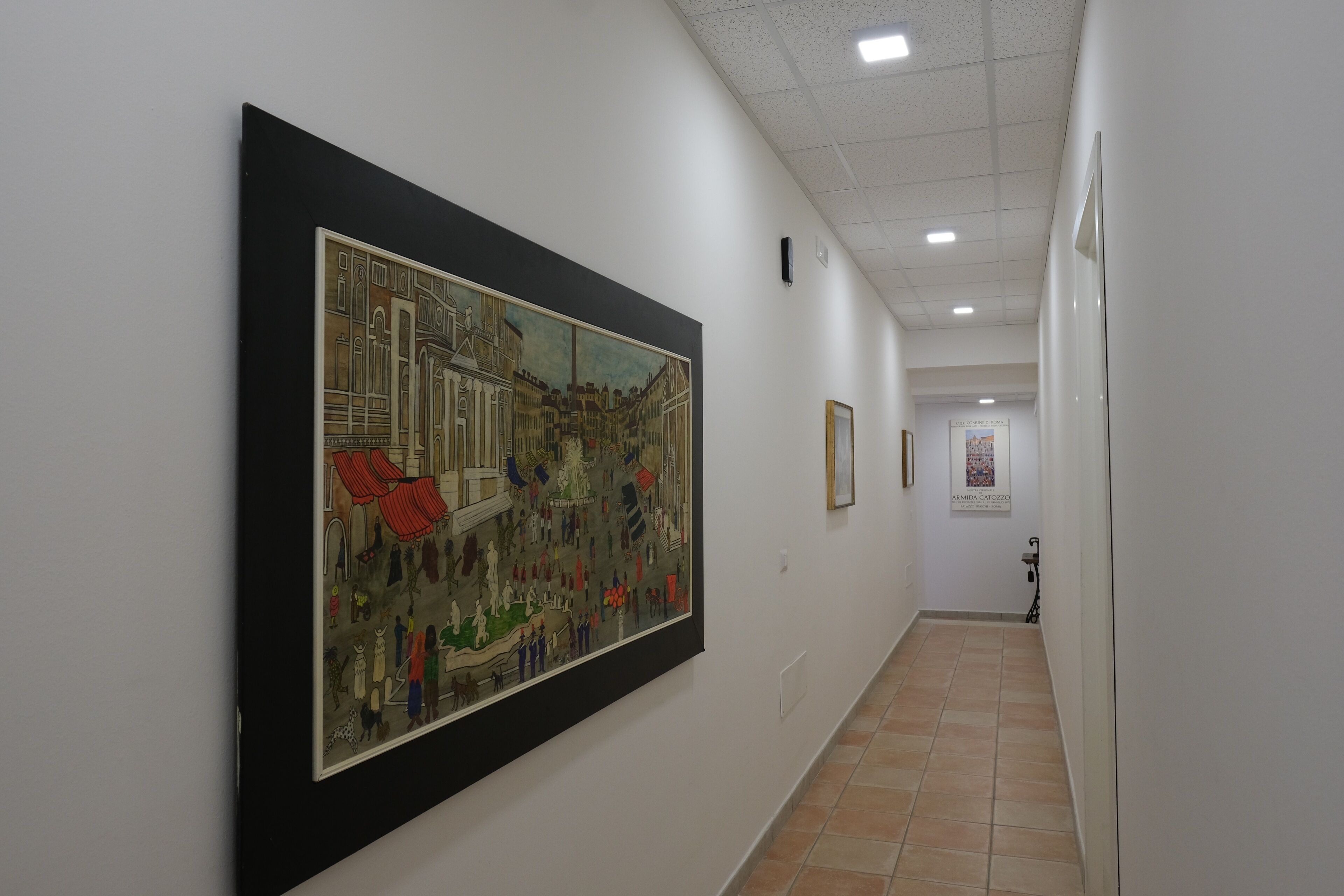 Un pasillo con una obra de arte grande enmarcada a la izquierda, suelo de baldosas y una puerta al final.