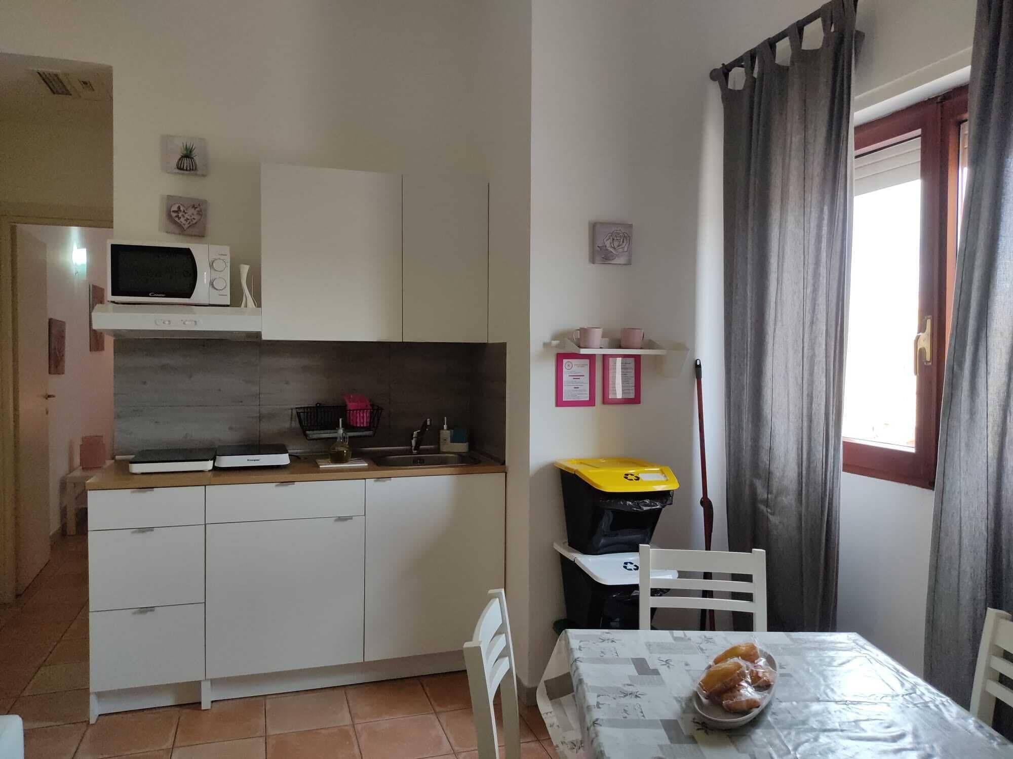 Een compacte keuken met witte kastjes, een magnetron, en een klein eethoekje met een tafel en stoelen.