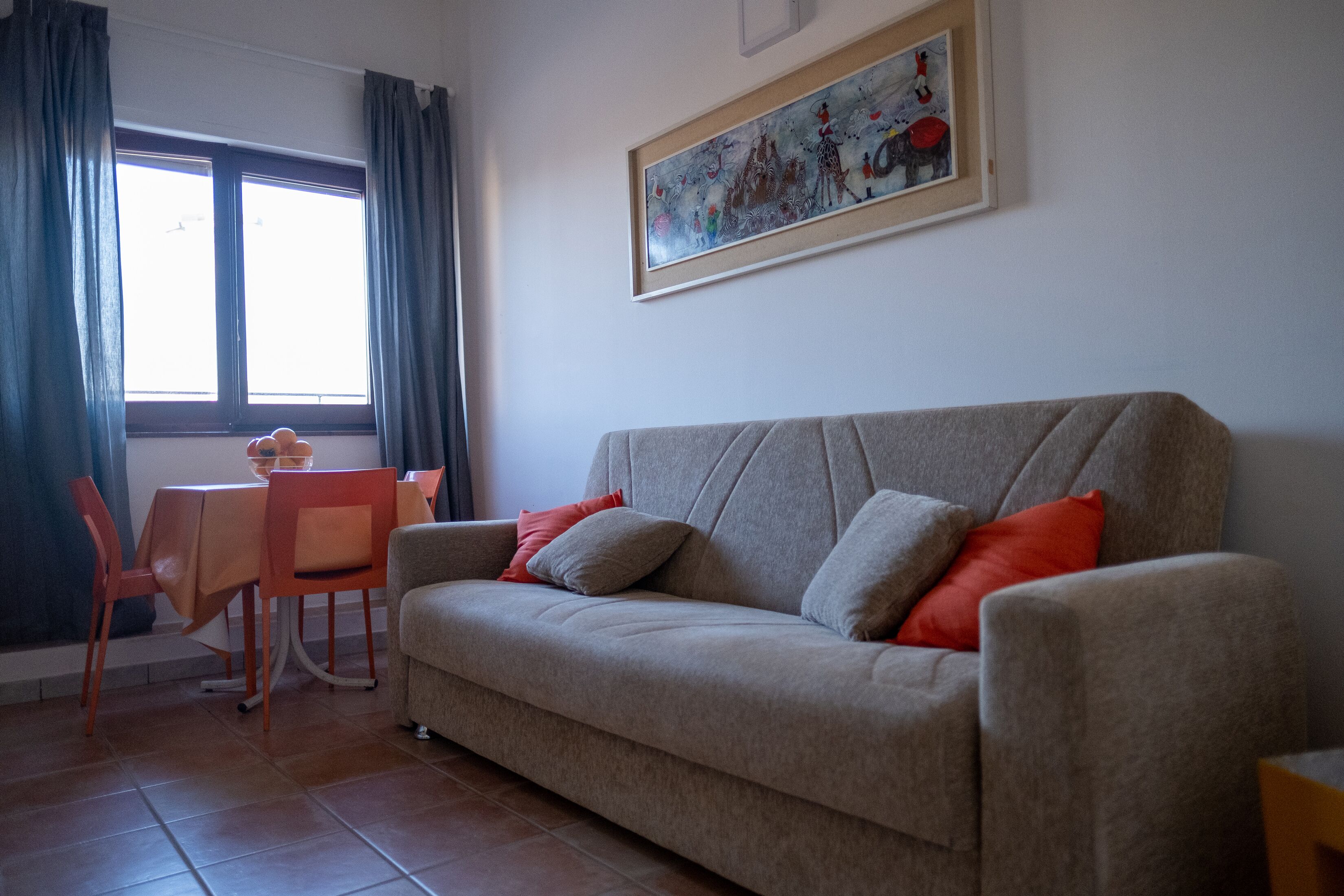 Un salon comprenant un canapé, une table à manger et des chaises. Il y a une fenêtre avec des rideaux et un tableau accroché au mur.
