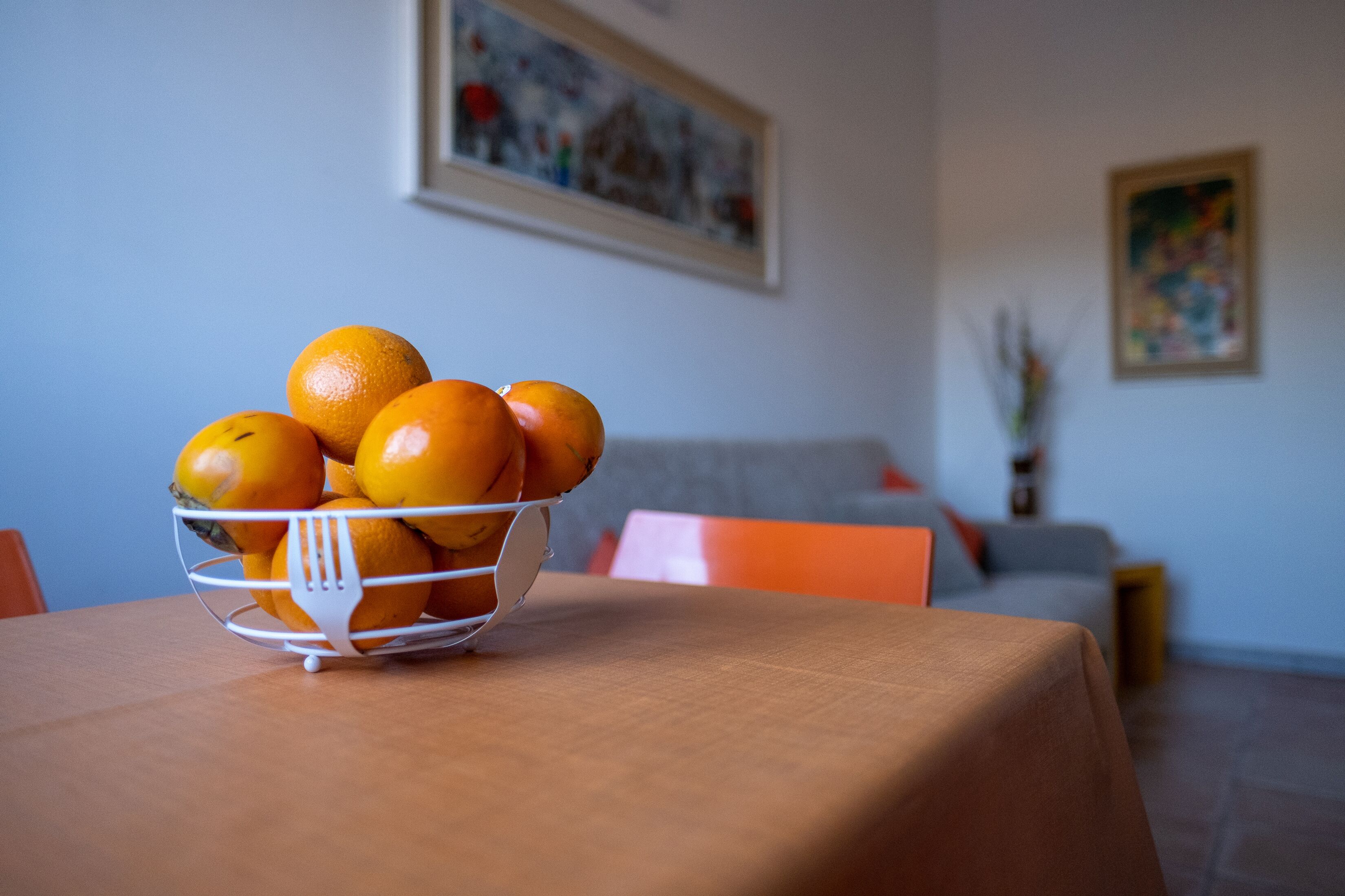 Uma mesa de jantar com uma cesta de frutas contendo laranjas.