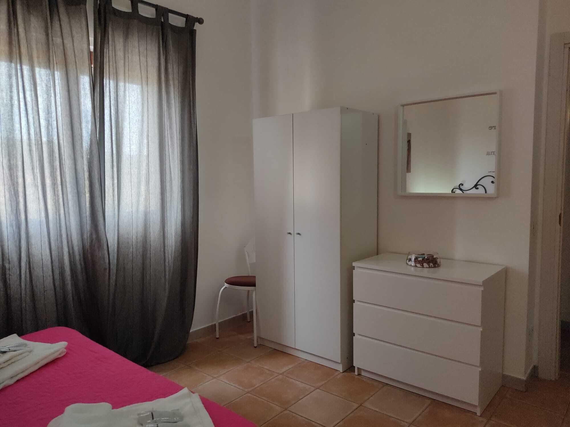 Una camera da letto con un letto, un armadio bianco, una piccola scrivania con uno specchio e una sedia.