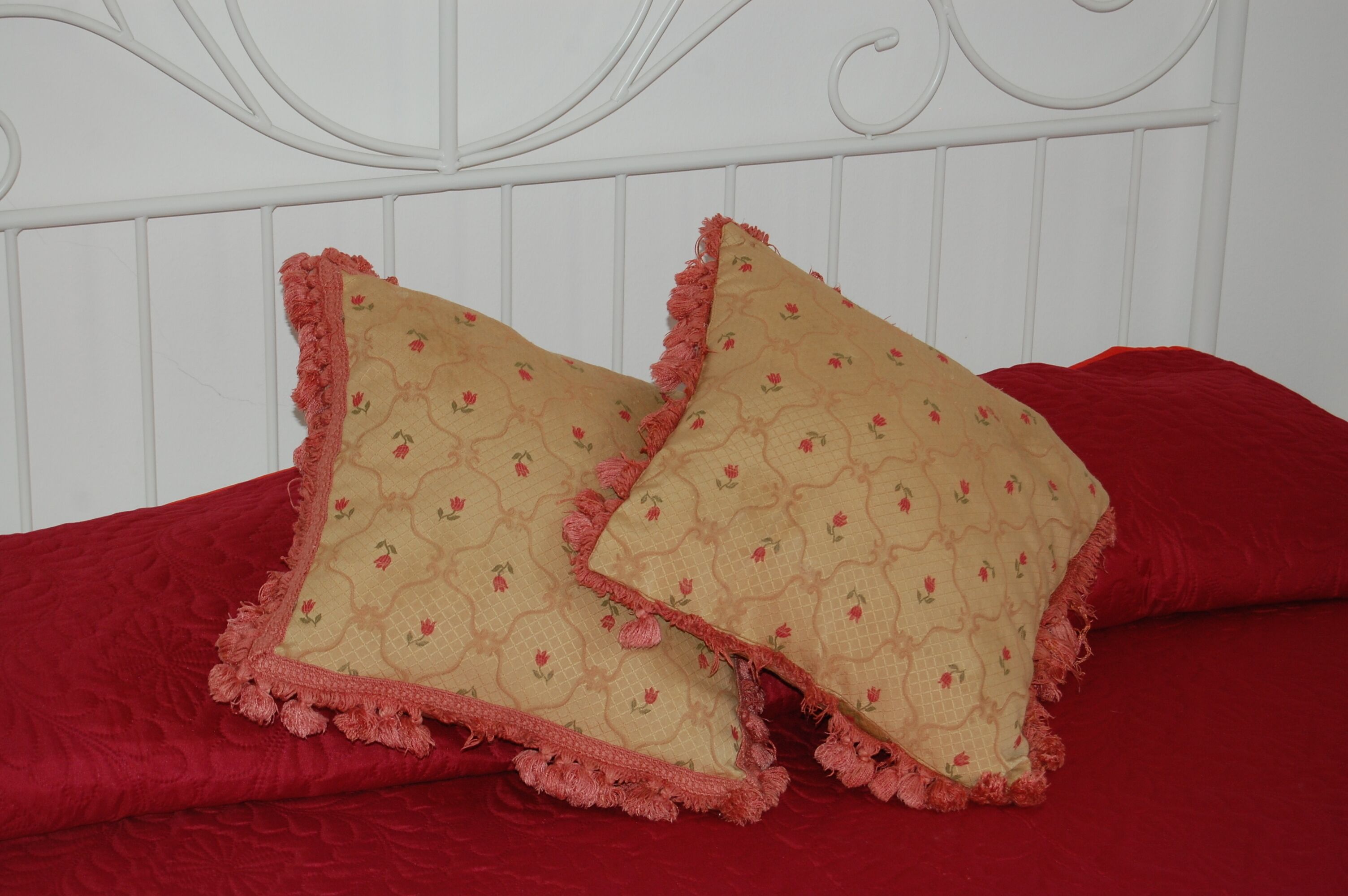 Una cama con ropa de cama roja y dos almohadas color beige con motivos florales.