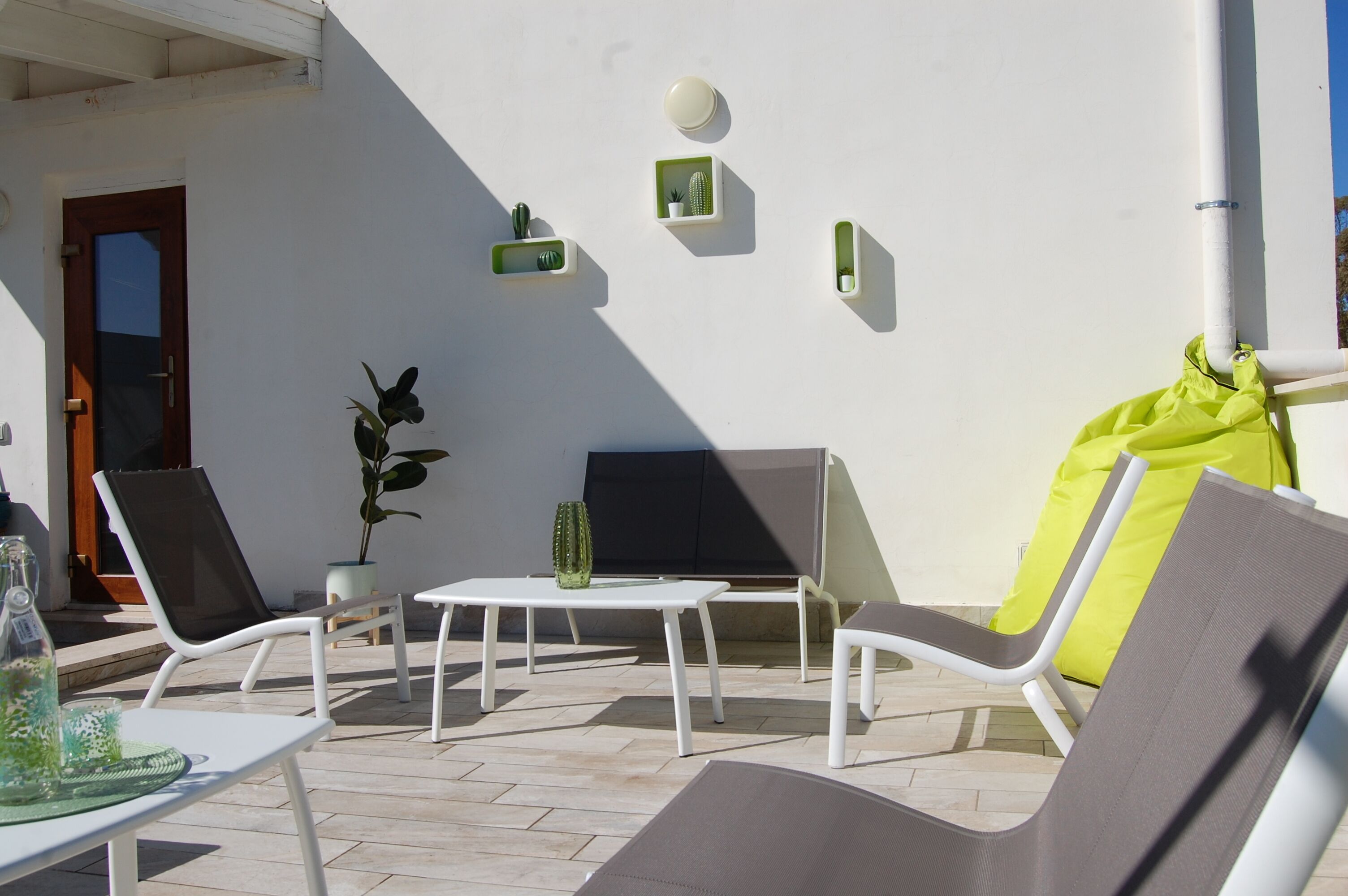 A sunlit outdoor seating area with white lounge chairs, a small table, and a potted plant.