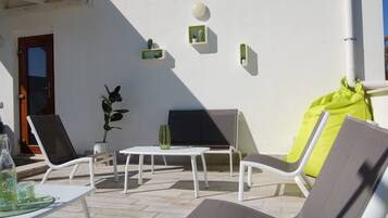 A sunlit outdoor seating area with white lounge chairs, a small table, and a potted plant.