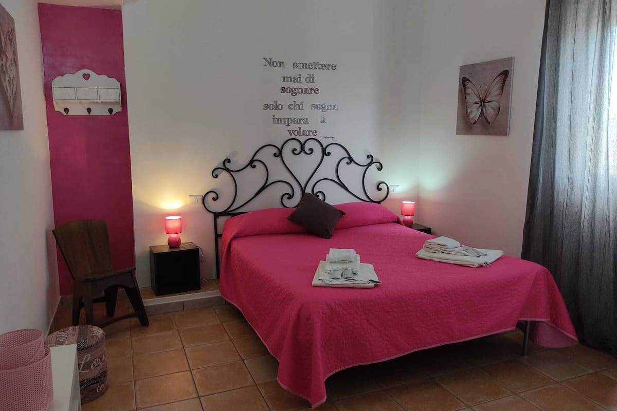 A bedroom with a bed, two bedside lamps, a chair, a wall decoration, and a butterfly painting.
