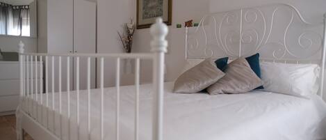 A bedroom with a white bed, white headboard, and a white crib.