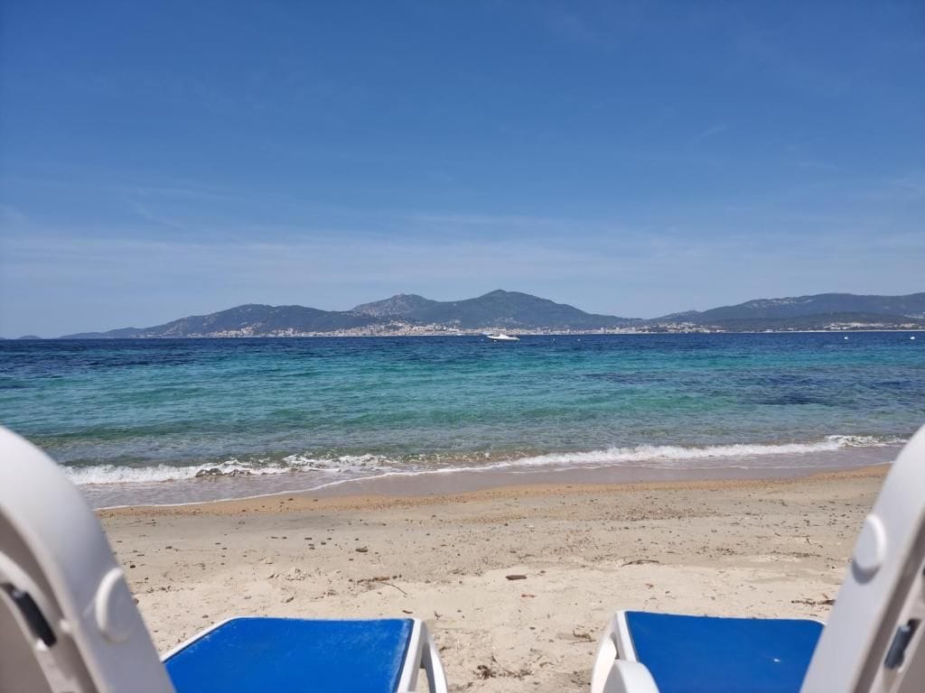 Une plage à l’eau d’un bleu cristallin, un rivage sablonneux et, au loin, une chaîne de montagnes.