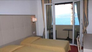 Una habitación con dos camas, una ventana con cortinas, una mesita y vista al mar.
