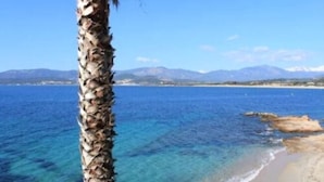 Vista costera con aguas azules cristalinas, una playa de arena y montañas al fondo.